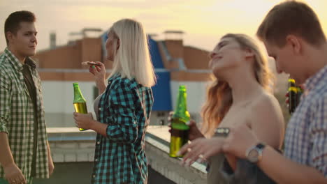 Two-young-couples-are-dancing-on-the-roof-and-eating-pizza-with-beer-on-the-party.-They-enjoy-moments-with-their-soul-mates-on-the-roof.